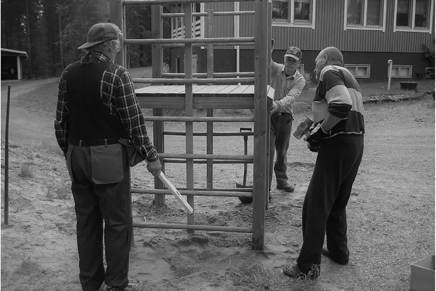 Kolme miestä kunnostavat lasten leikkipaikka pihalla